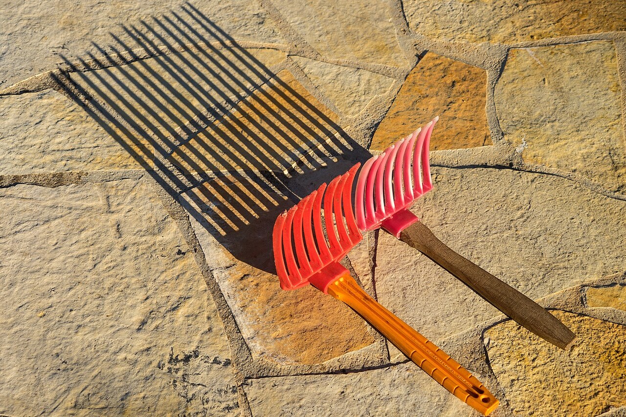 Two plastic olive harvest combs with wooden handles lying on stone paving