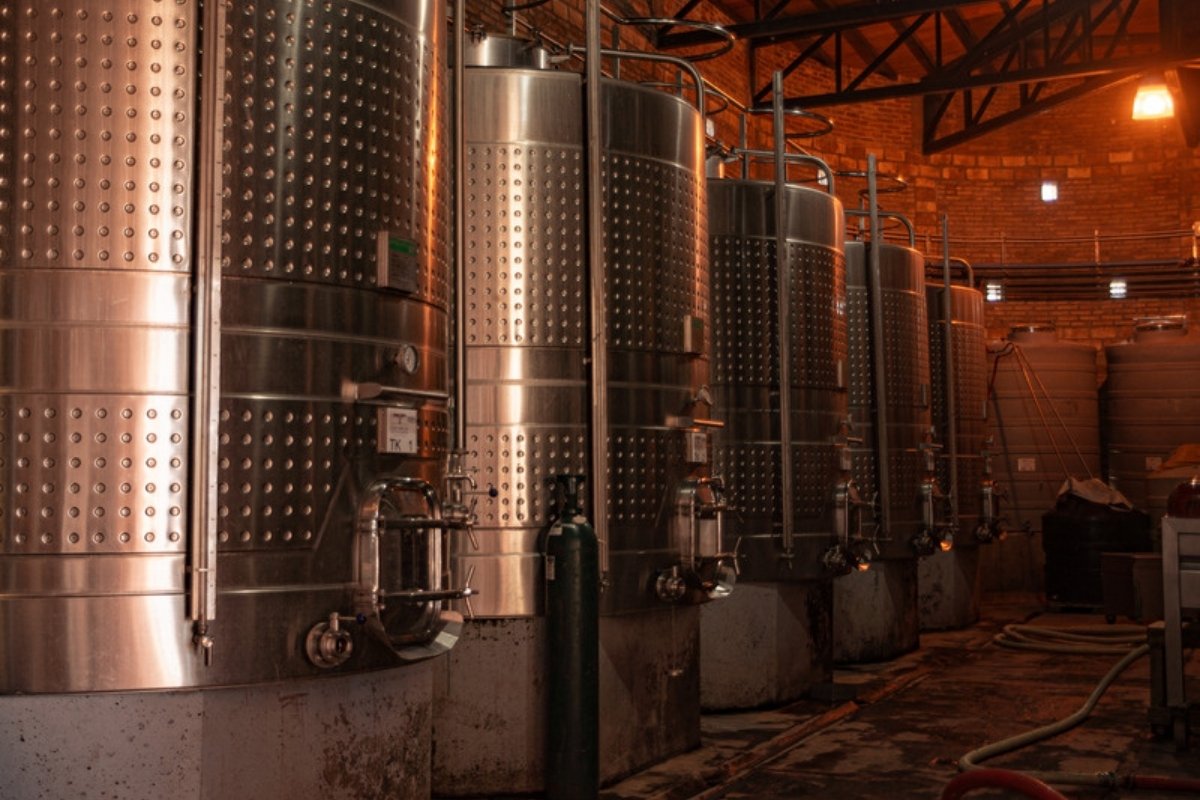 Row of stainless steel storage tanks in a dimly lit storage hall